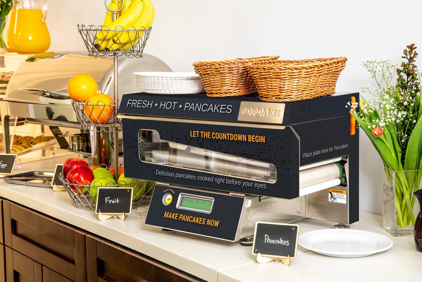 Popcake pancake machine op een ontbijtbuffet, met de knop om pancakes te maken en borden ernaast